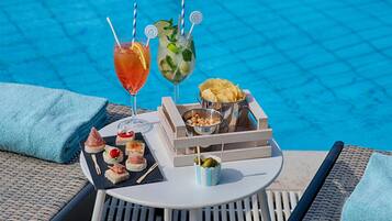 A poolside table with drinks, snacks, and a tray of appetizers.