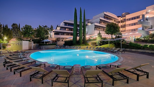 Une piscine entourée de chaises longues et un bâtiment moderne à plusieurs étages, doté de balcons.