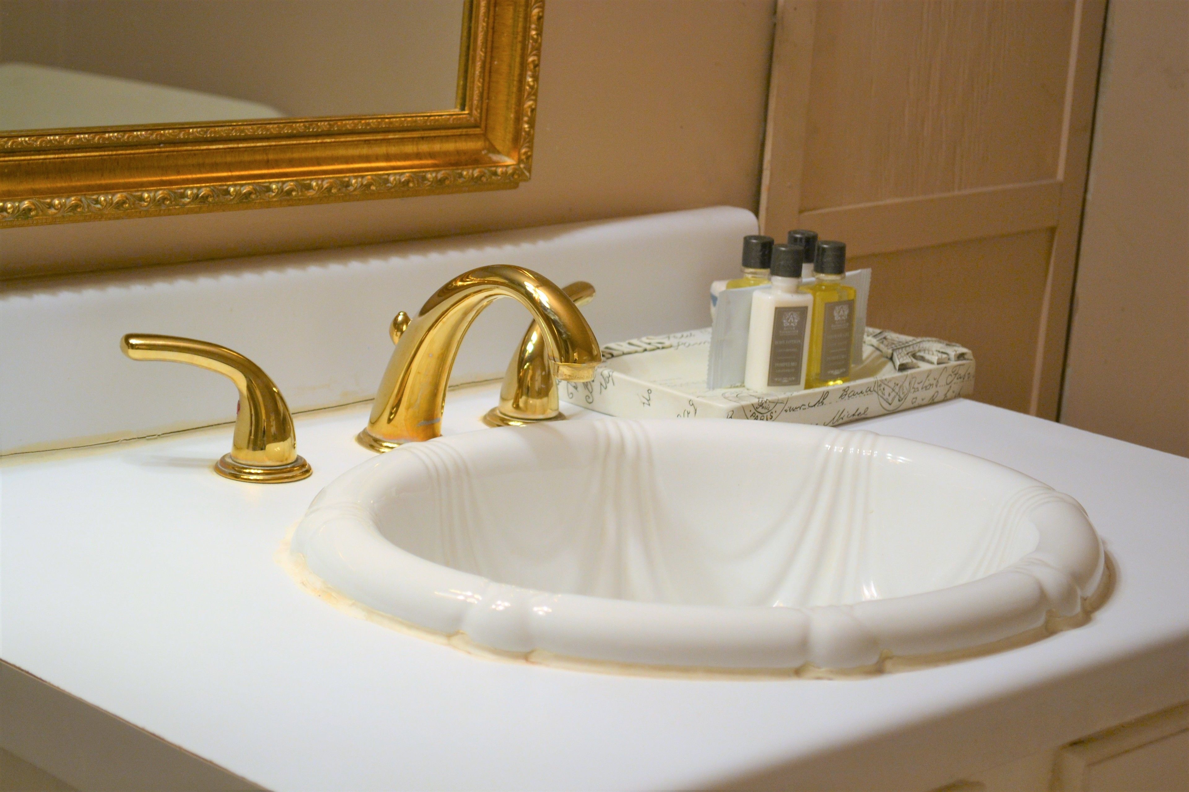 A bathroom sink with a gold faucet, a marble countertop, and a tray holding toiletries.