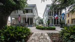 A courtyard with two-story buildings, a cobblestone path, and flags. - Degas House (New Orleans)