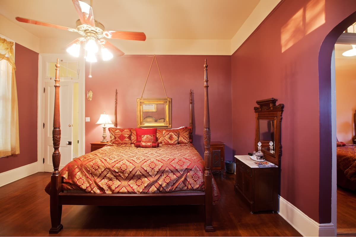 Un lit à baldaquin avec quatre poteaux, un ventilateur de plafond et une table de chevet avec une lampe.