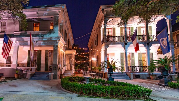 A historic building with a front porch, outdoor seating, and flags. - Degas House (New Orleans)