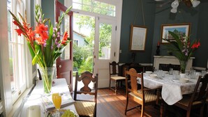 A dining room with a table set for four, chairs, a vase with flowers, and a view through an open door. - Degas House (New Orleans)