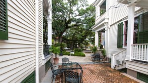A courtyard with a brick floor, outdoor seating, and white buildings with green shutters. - Degas House (New Orleans)
