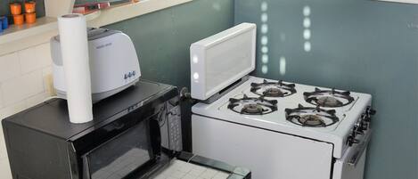 Cozinha compacta com micro-ondas, fogão e bancada pequena.