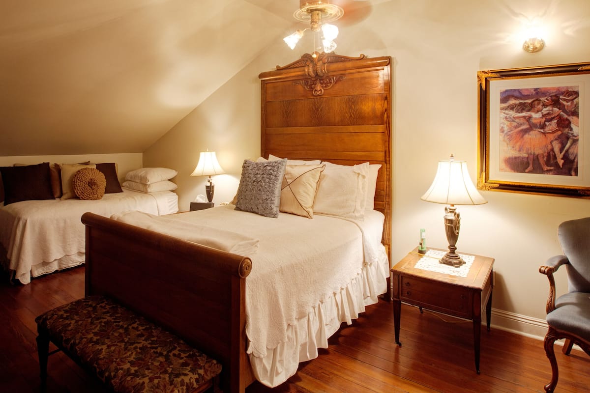 Une chambre à coucher avec deux lits, une tête de lit en bois, une table de chevet, une chaise et un tableau accroché au mur.
