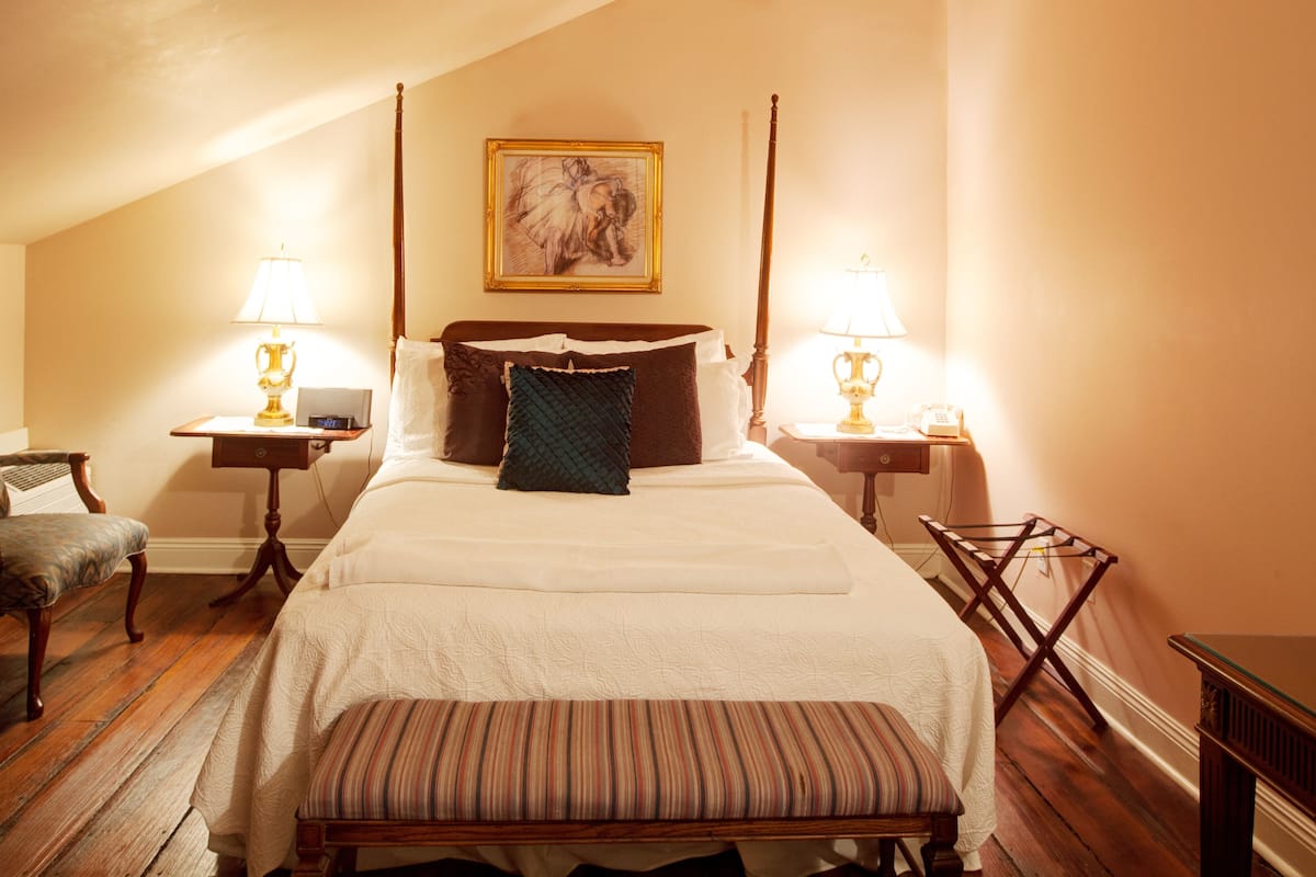 Une chambre d’hôtel avec un lit à baldaquin, une télévision, un bureau avec une lampe et une chaise.