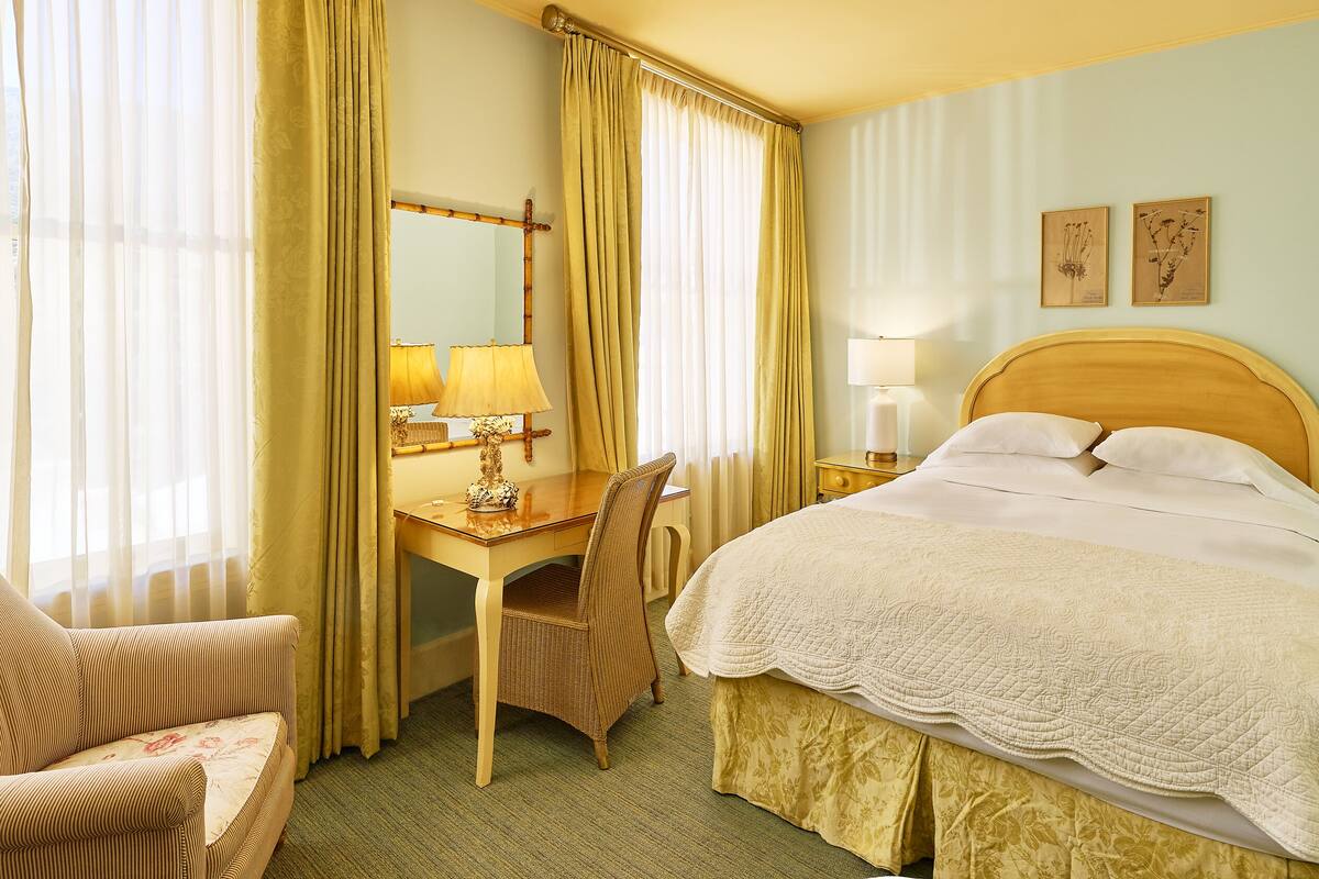 Habitación de hotel con cama, escritorio, silla, lámpara y dos cuadros en la pared.