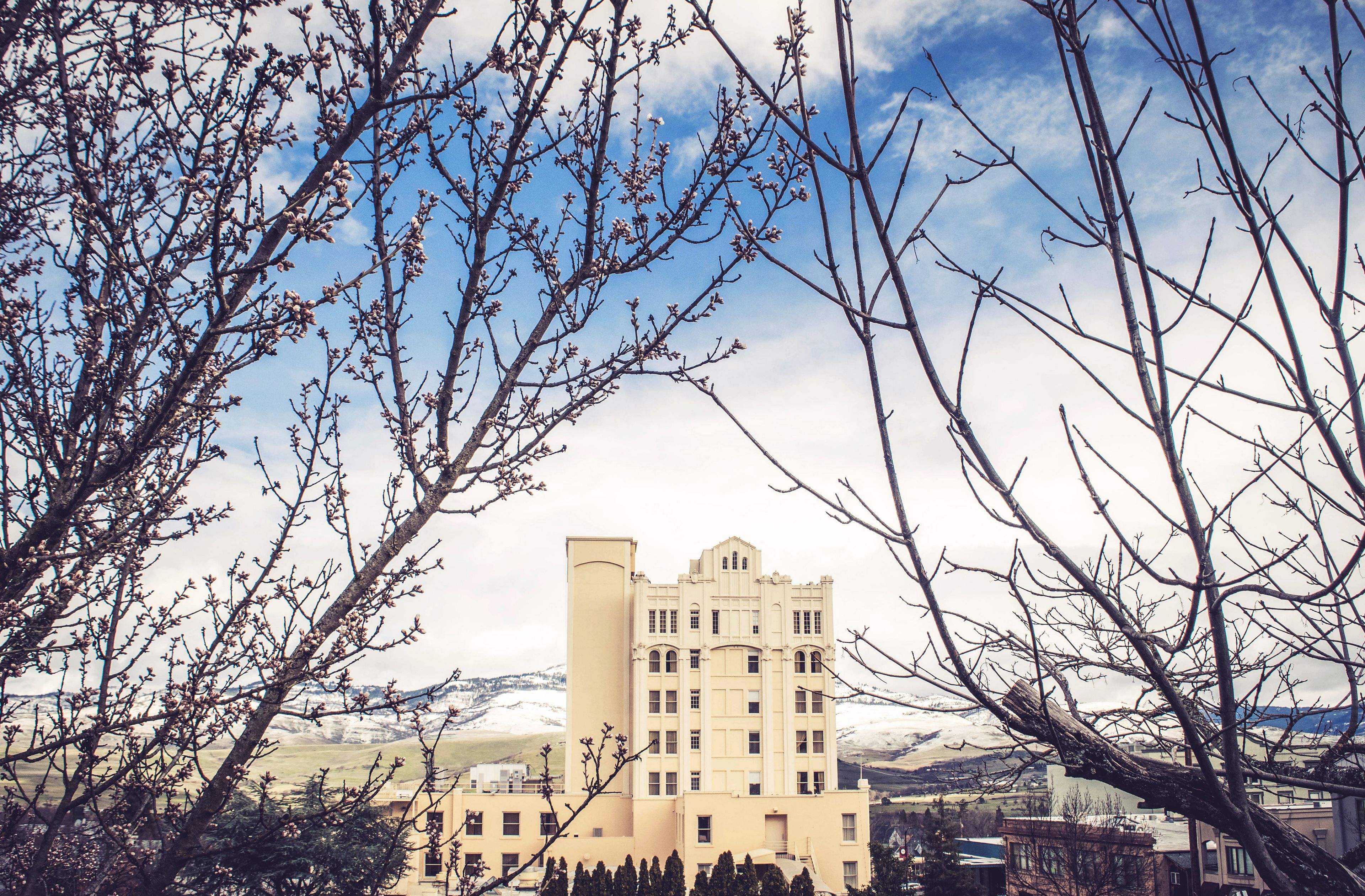 A large, multi-story building with a symmetrical facade and a central tower, surrounded by trees and a mountainous landscape.