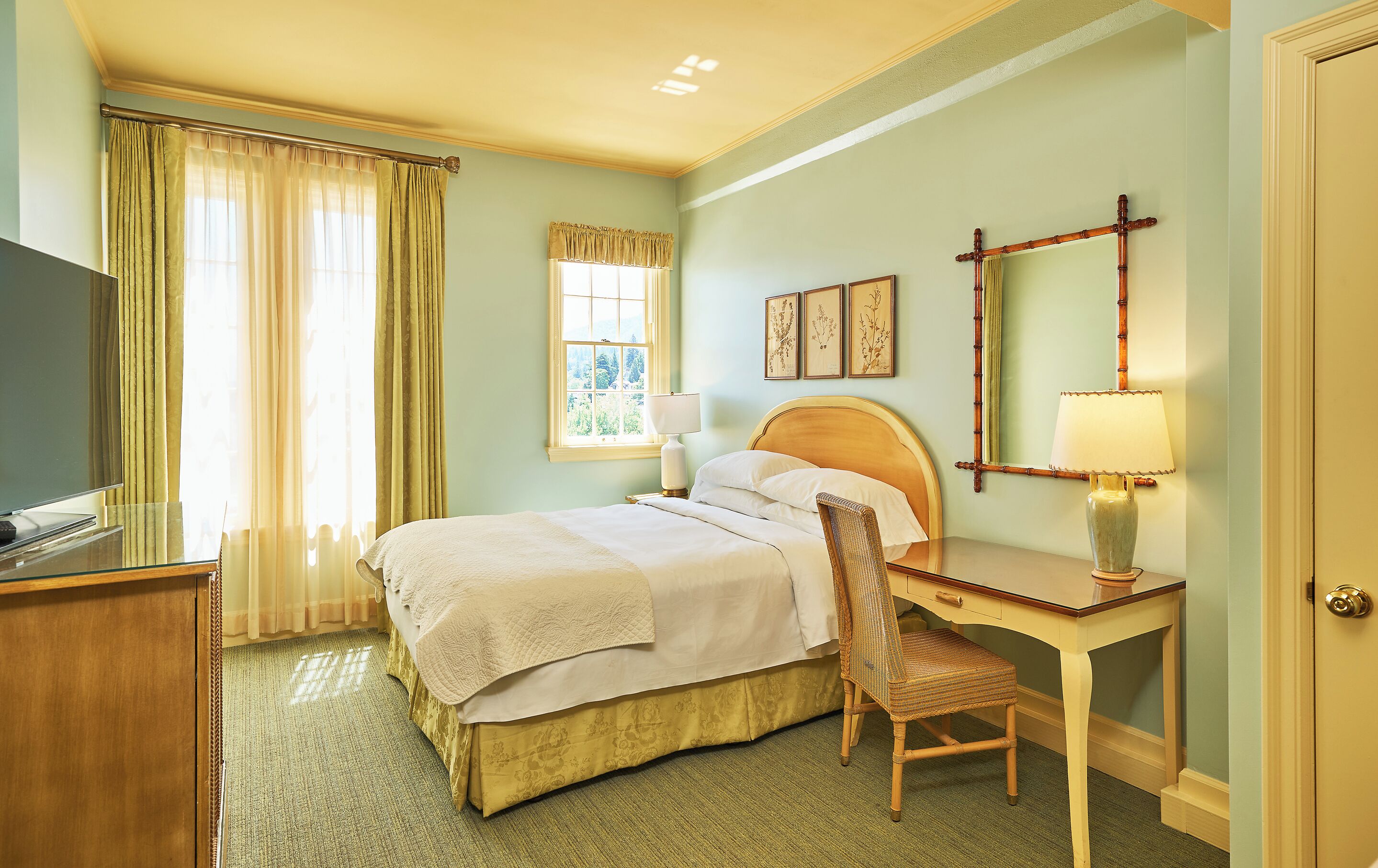 A hotel room with a bed, a desk, a chair, a television, and a window with curtains.