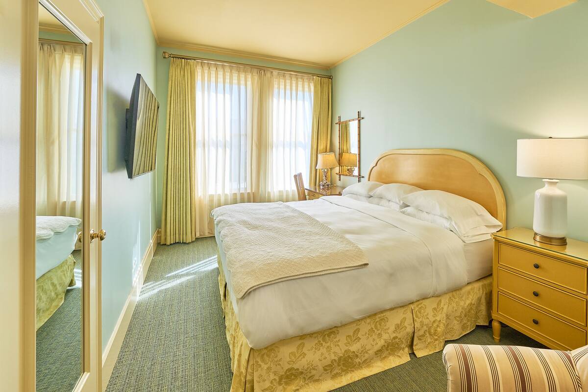 Una habitación de hotel con una cama grande, una mesita de noche con lámpara, una silla y un espejo.