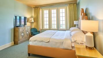 A hotel room with a bed, a television, a desk with a lamp, and a chair.