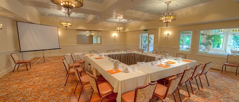 A conference room with a long table, chairs, a projector screen, and chandeliers.