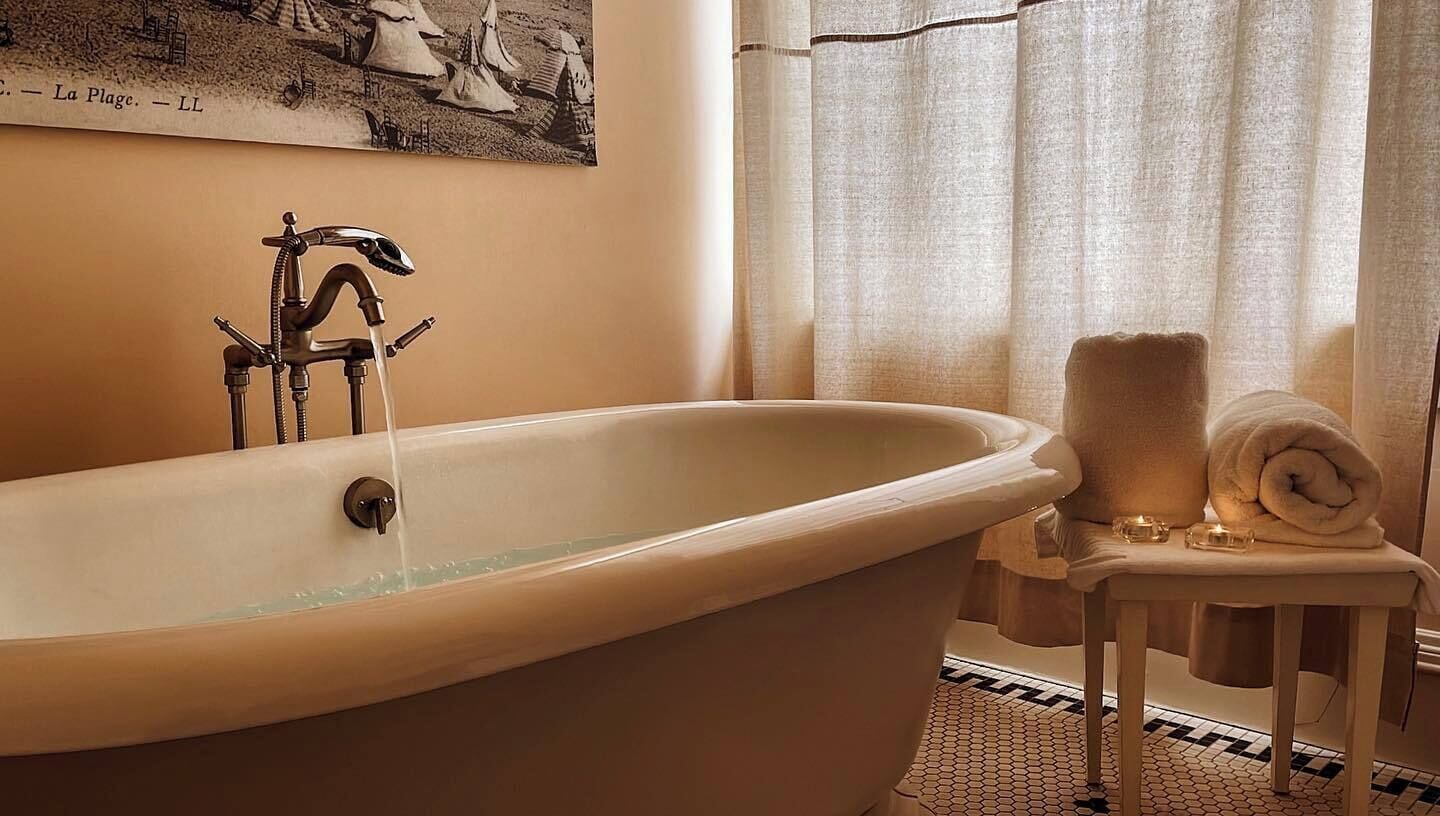 Ein Badezimmer mit einer freistehenden Badewanne, einem Handtuchhalter mit Handtüchern und einem Vintage-Poster an der Wand.