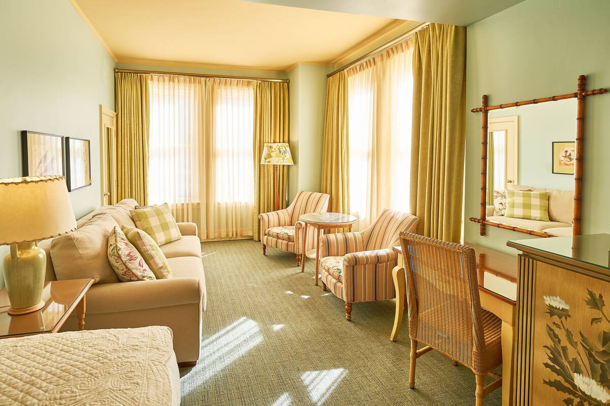 Habitación de hotel con sofá, sillones, una mesita, lámpara y espejo.