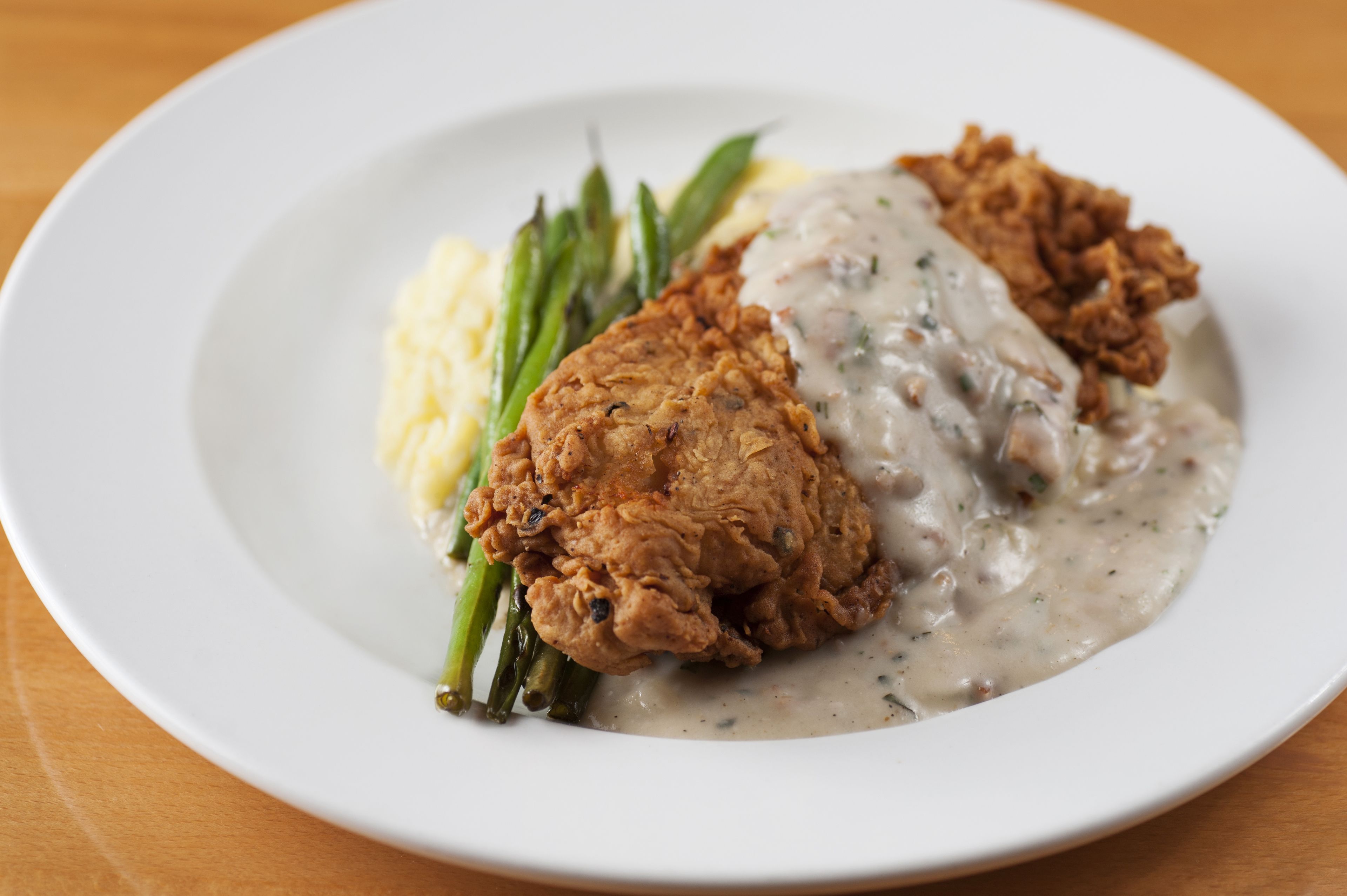 Ein Teller mit gebratenem Hähnchen, Kartoffelpüree und grünen Bohnen.