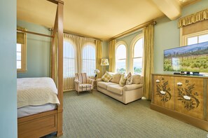 A bedroom with a four-poster bed, a sitting area with a sofa and armchair, and a television on a cabinet. - Ashland Springs Hotel (Ashland)