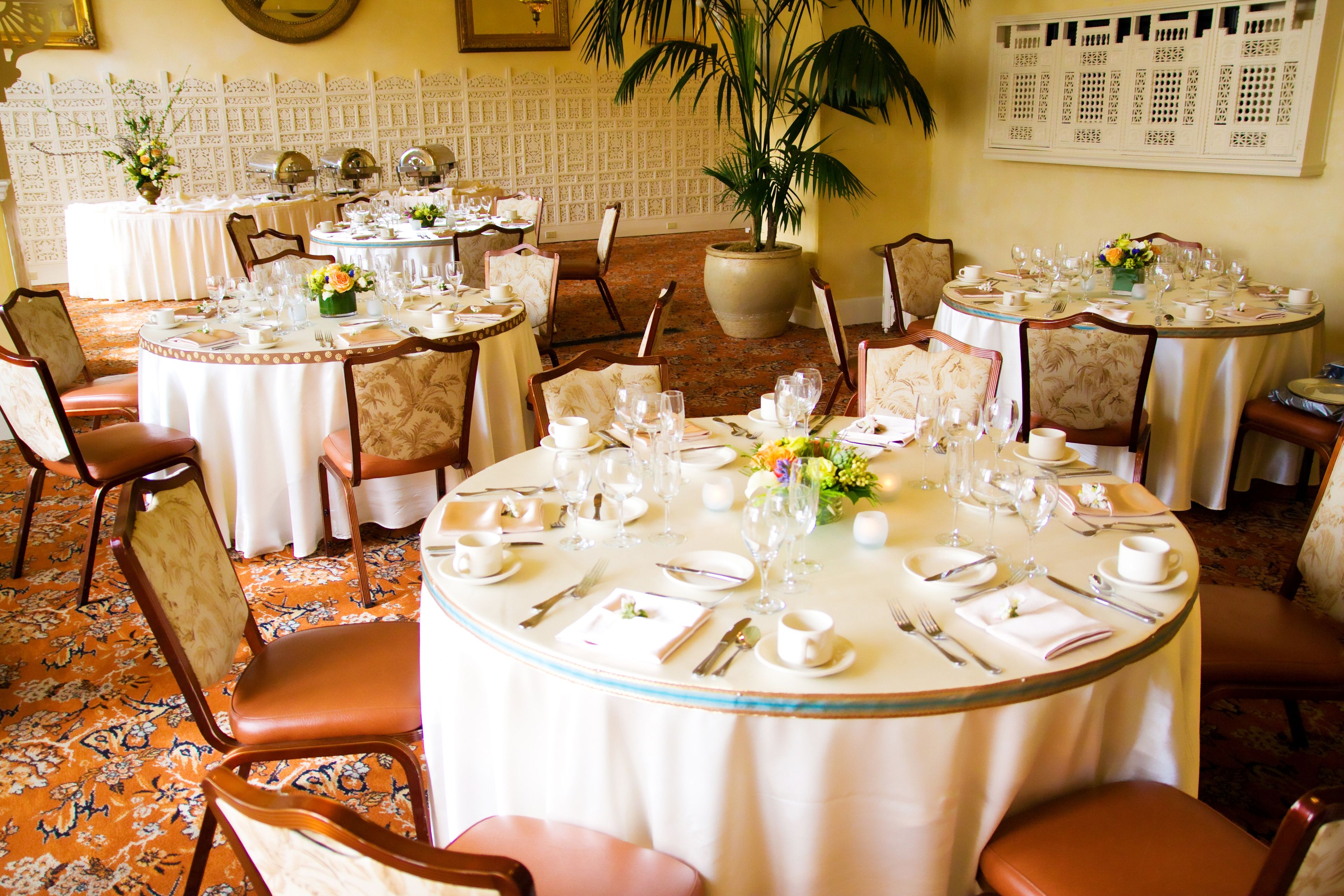 Ein Hotelrestaurant mit mehreren runden Tischen, gedeckt für das Abendessen, jeweils mit Stühlen und Geschirr.