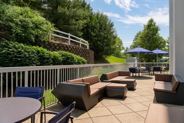 An outdoor patio area with a sectional sofa, round tables, and umbrellas.