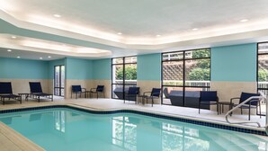 An indoor swimming pool with clear blue water, surrounded by lounge chairs and tables, and large windows offering views of greenery outside. - SpringHill Suites by Marriott West Mifflin (West Mifflin)