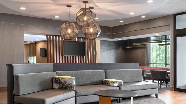 A modern living area with a sectional sofa, a round coffee table, and a flat-screen TV mounted on a wooden panel wall. - SpringHill Suites by Marriott West Mifflin (West Mifflin)