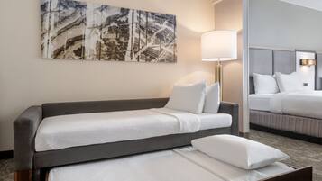Habitación de hotel con sofá cama, una cama separada, una lámpara y un cuadro abstracto grande en la pared.