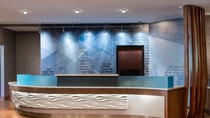 A reception desk with a modern design, featuring a curved shape and a textured white base. - SpringHill Suites by Marriott West Mifflin (West Mifflin)
