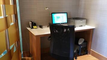 Een kleine kantoorruimte met een bureau, stoel, computer, printer en een lamp.