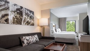 A hotel room with a sofa, a bed, a bedside table, a lamp, a TV, and a large abstract painting on the wall. - SpringHill Suites by Marriott West Mifflin (West Mifflin)