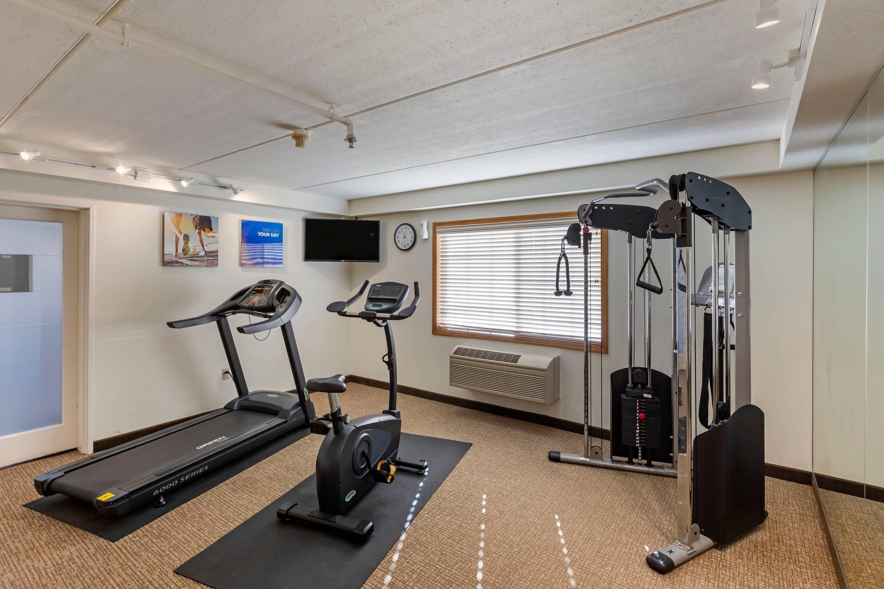 Une salle de sport équipée d’un tapis de course, d’un vélo elliptique et d’appareils de musculation.