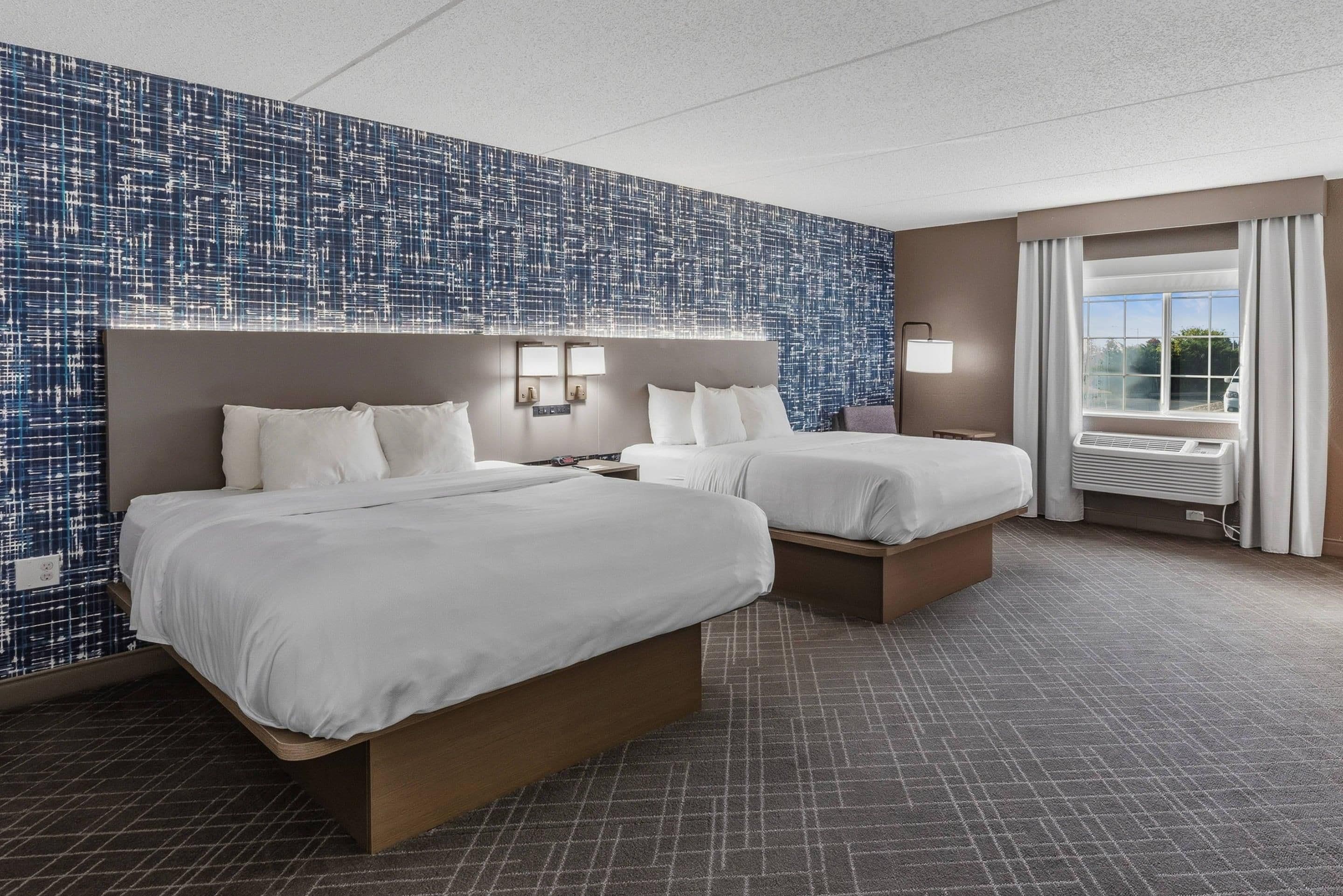 A hotel room with two beds, a large window with curtains, and a patterned wall.