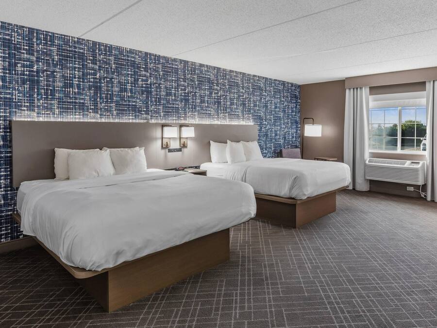Une chambre d’hôtel avec deux lits, une grande fenêtre avec des rideaux et un mur décoré d’un motif.