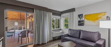 Una sala de estar moderna con un sofá gris, una mesita auxiliar amarilla y un ventanal de vidrio que da a una piscina.