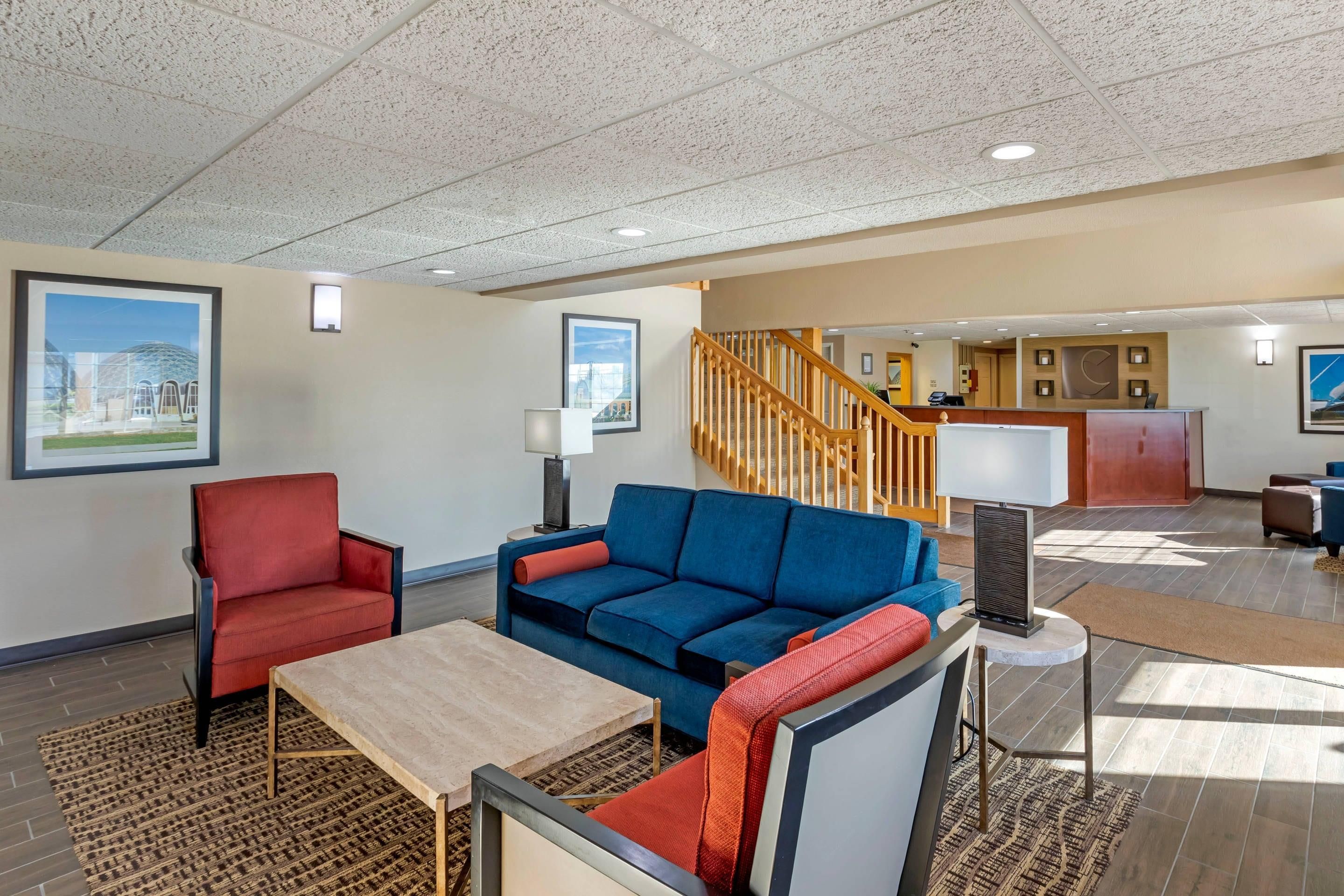 A hotel lobby with a reception desk, a staircase, and seating areas with a red and blue sofa.