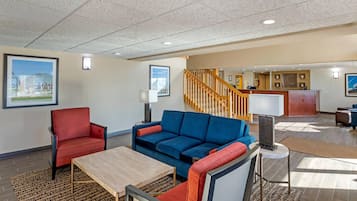 A hotel lobby with a reception desk, a staircase, and seating areas with a red and blue sofa.