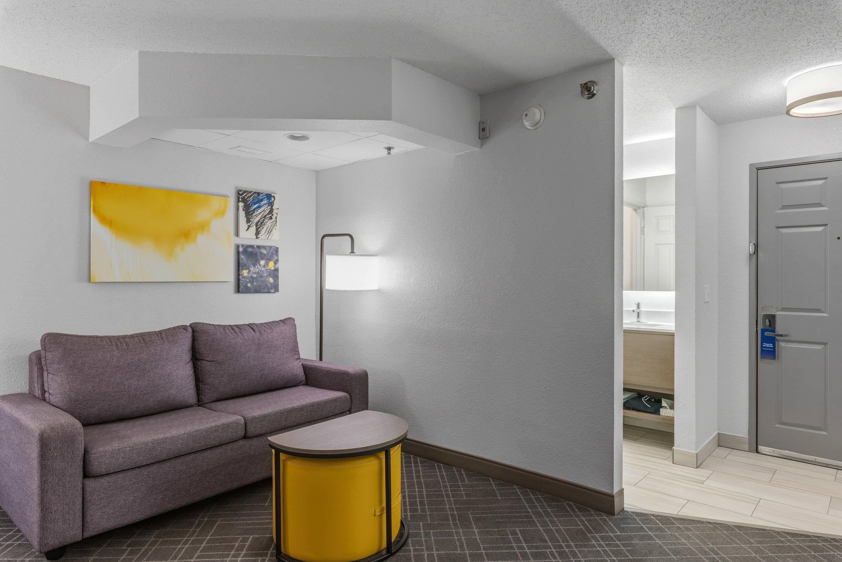Un hall d’hôtel avec un canapé gris, une petite table jaune et des œuvres d’art accrochées au mur.