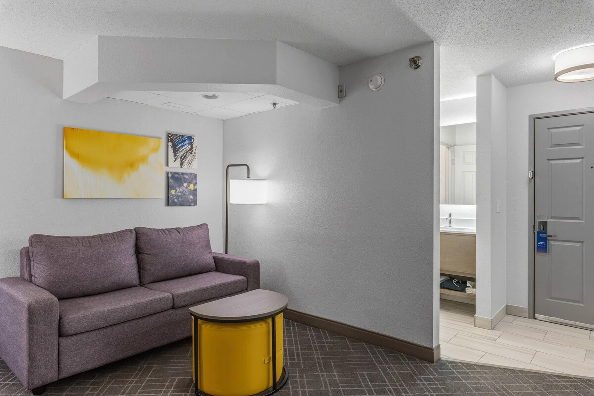 A hotel lobby with a gray sofa, a small yellow table, and artwork on the wall.