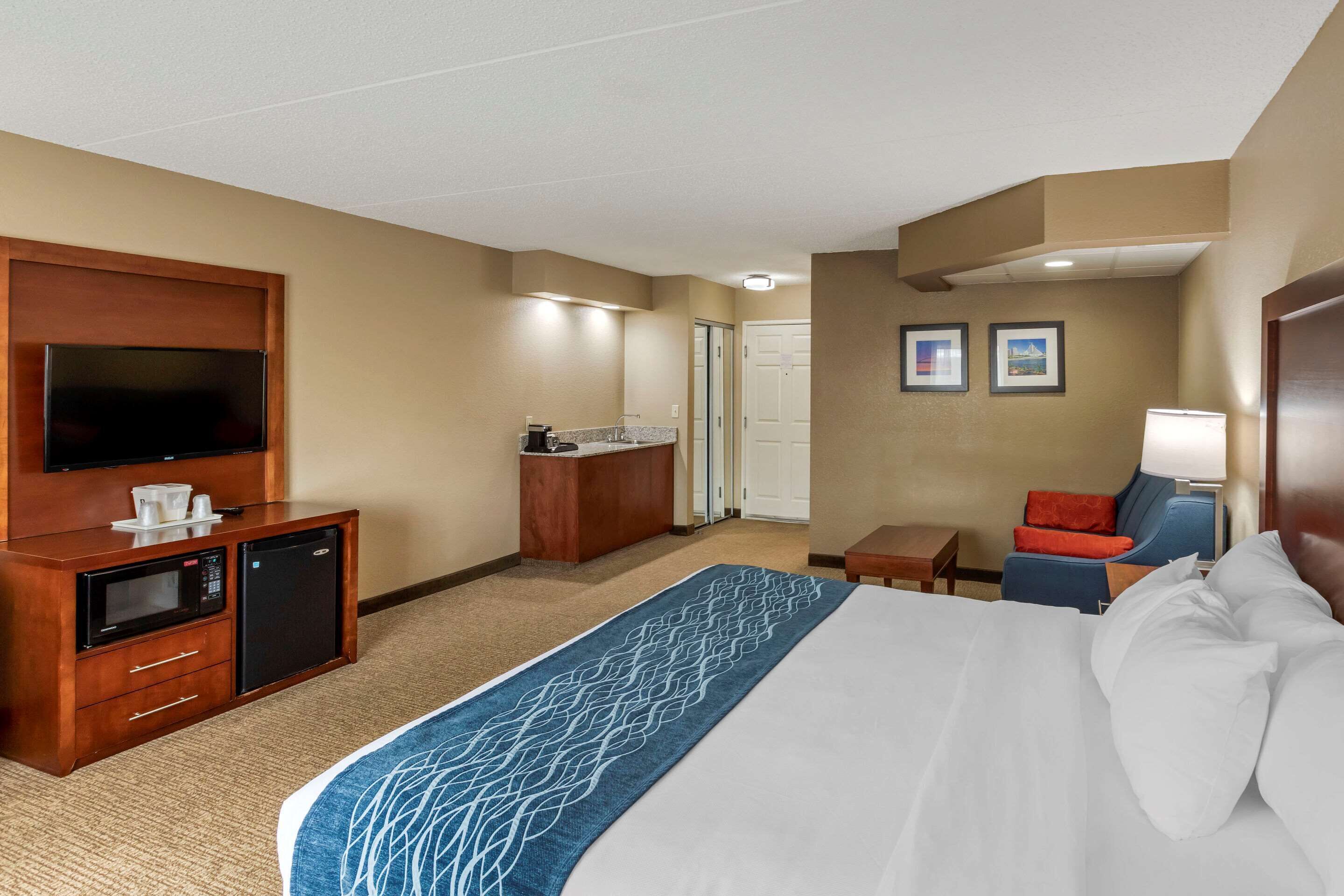 A hotel room with a large bed, a desk with a microwave, a television, and a small seating area with a chair and table.