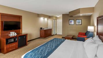 A hotel room with a large bed, a desk with a microwave, a television, and a small seating area with a chair and table.