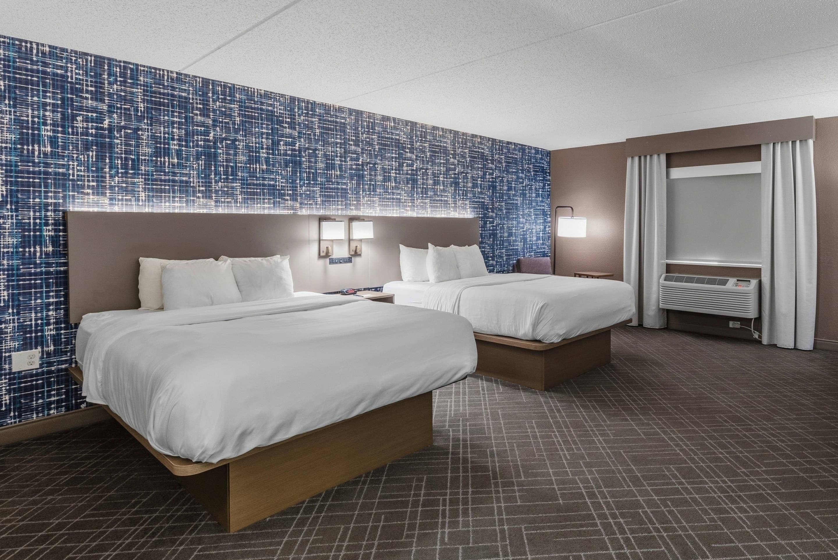 Habitación de hotel con dos camas, un mural grande en la pared, un espejo y una ventana con cortinas.