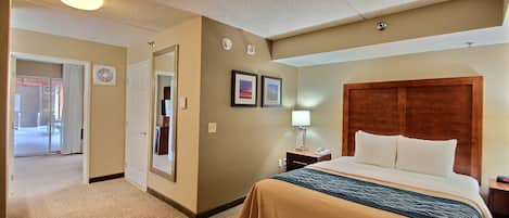A hotel room with a large bed, a nightstand, a lamp, and a door leading to a hallway.