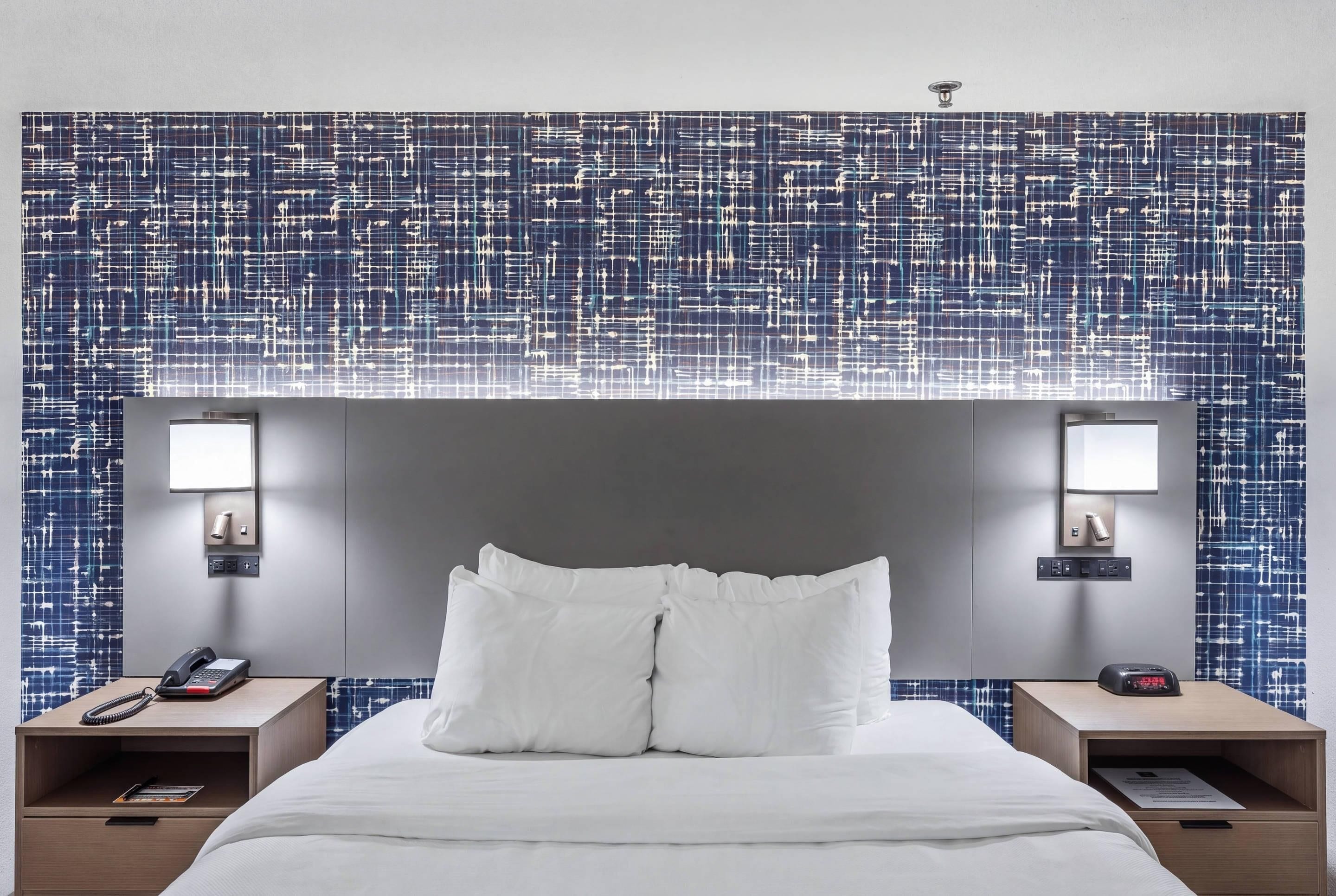 Ein Hotelzimmer mit einem großen Bett, zwei Nachttischen, einer Wandlampe und einer Wand mit Muster.