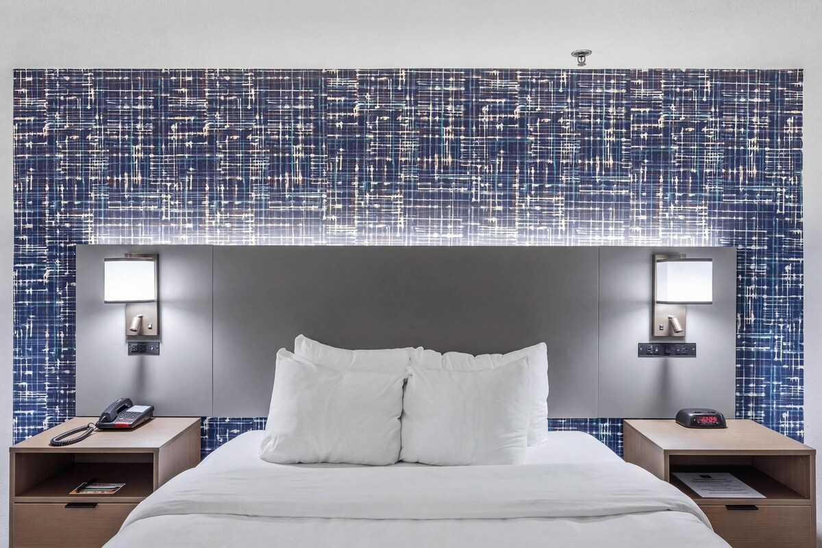 A hotel room with a large bed, two bedside tables, a wall-mounted lamp, and a patterned wall.