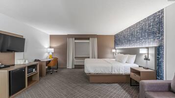 A hotel room with a bed, desk, chair, television, and a large abstract wall art piece.