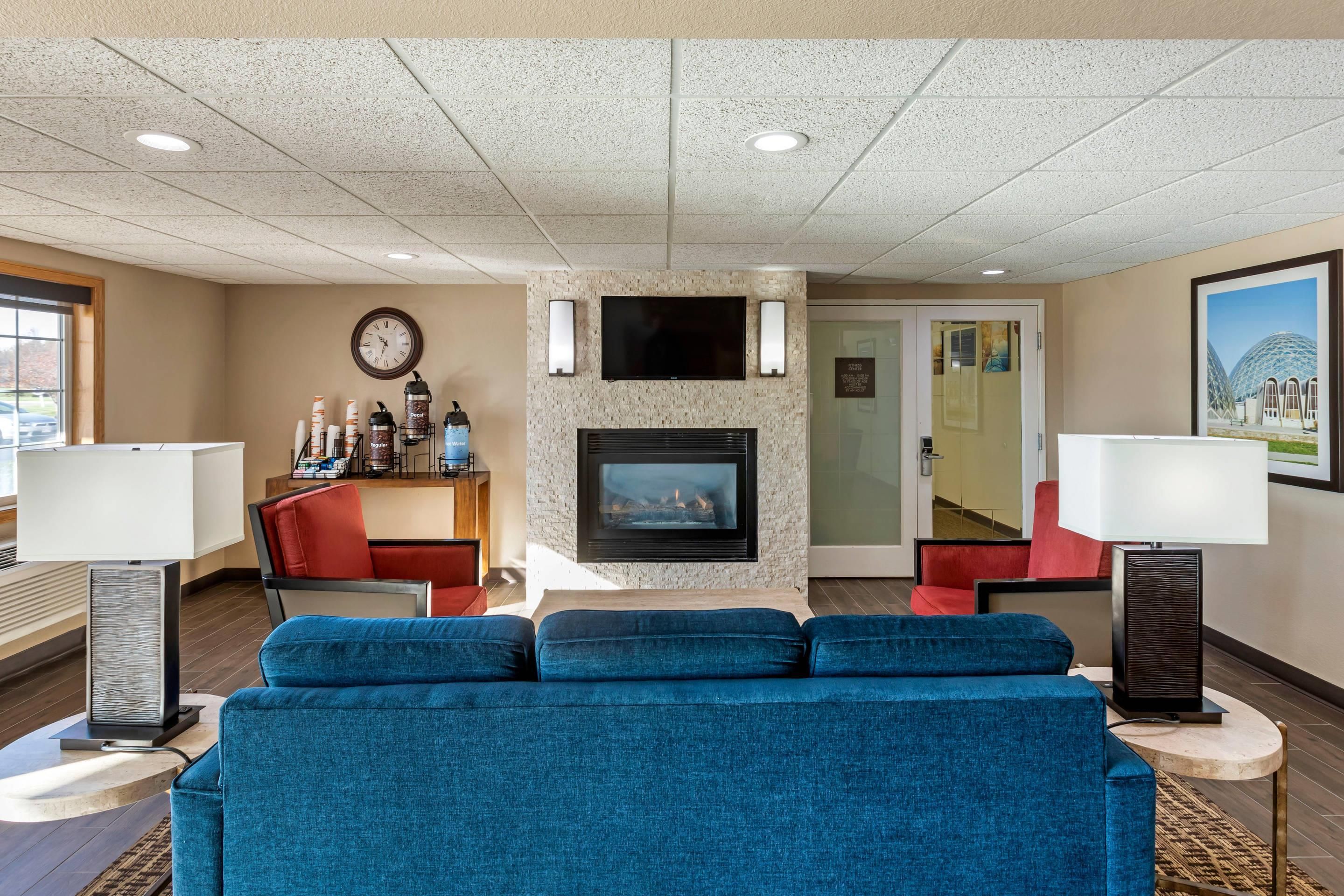 A hotel lobby with a blue sofa, a fireplace, a clock, and a coffee station.