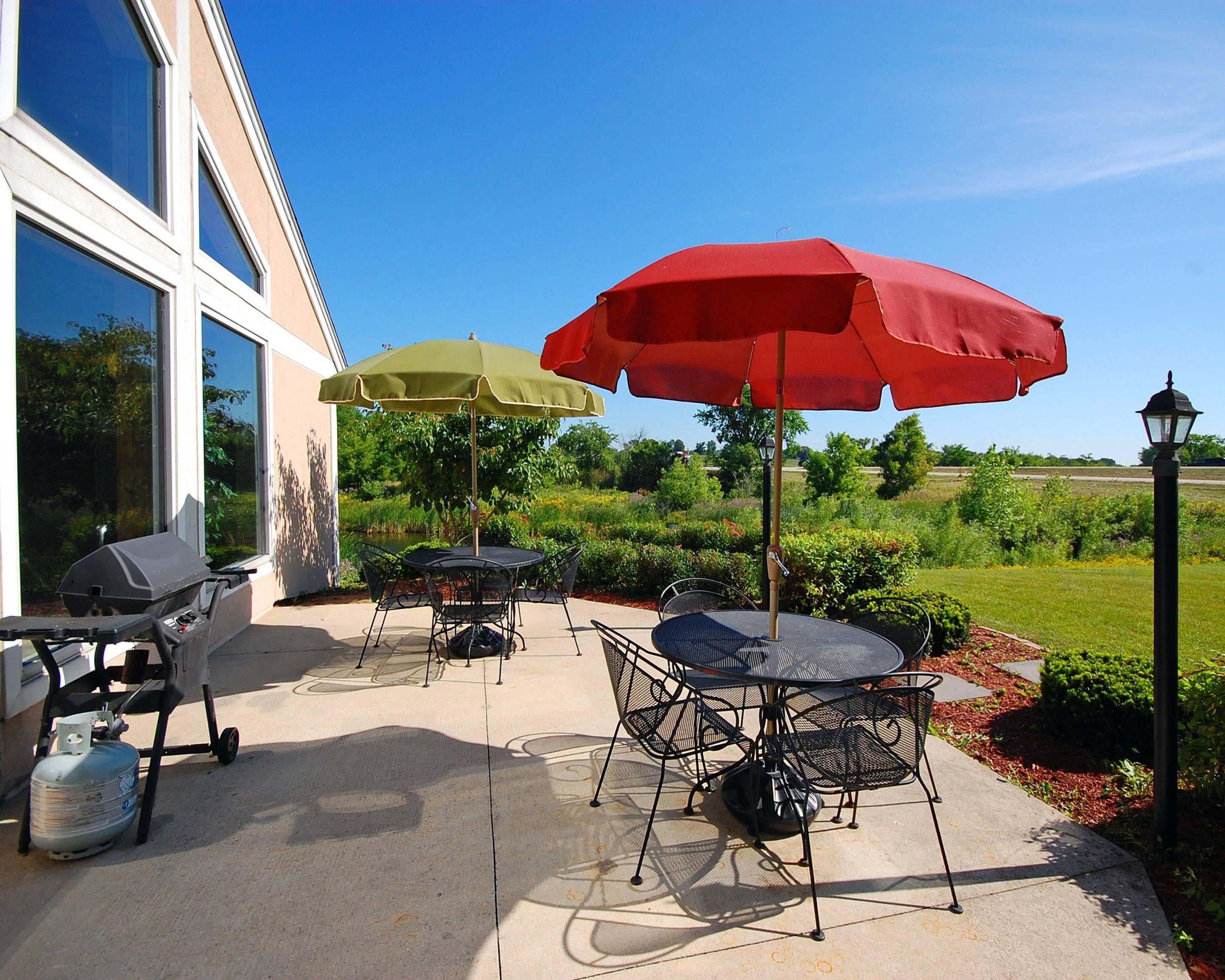 Une terrasse extérieure équipée d’un barbecue, de tables, de chaises et de parasols.