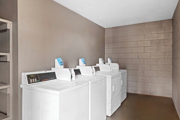 Une buanderie équipée de quatre machines à laver et de quatre sèche-linge blancs, d’un panneau de commande et d’un mur en briques.