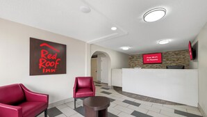 Un vestíbulo de Red Roof Inn con un mostrador de recepción, dos sillones rojos y una pequeña mesa.