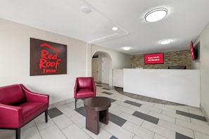 A Red Roof Inn lobby with a reception desk, two red armchairs, and a small table. - Red Roof Inn Charlotte - Airport (Charlotte)