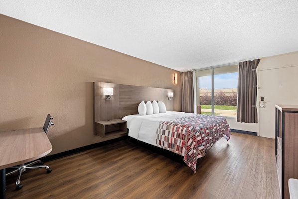 Habitación de hotel con cama, escritorio, silla, mesita de noche y un amplio ventanal con cortinas.